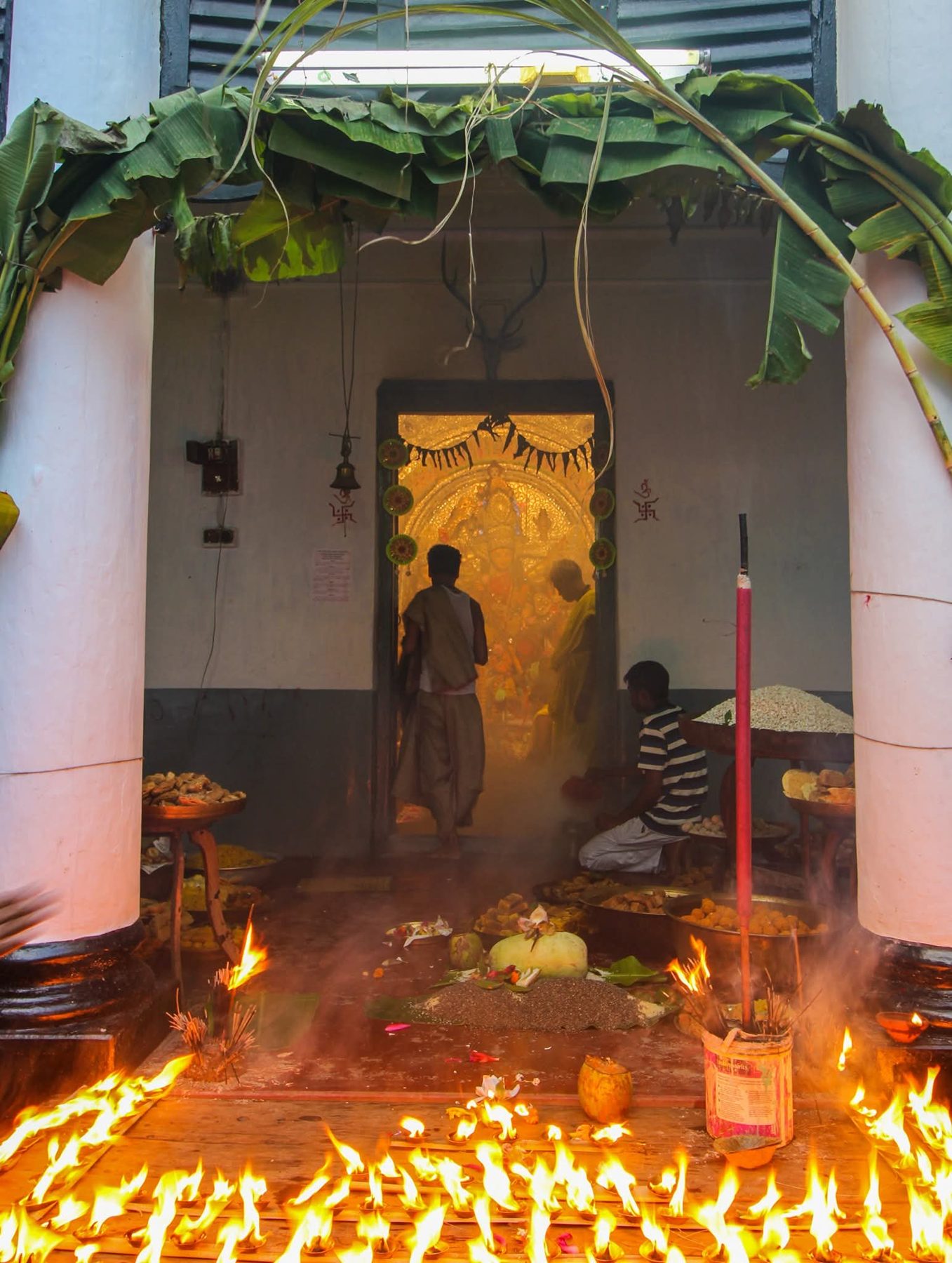 Sanctum doorway framed with banana leaves, lamps burning in front